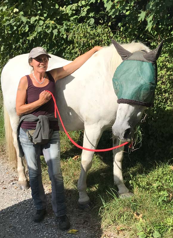 jeannette-karlen2 Jeannette Karlen steht neben einem Schimmel und hat den linken Arm auf seinen Rücken gelegt.